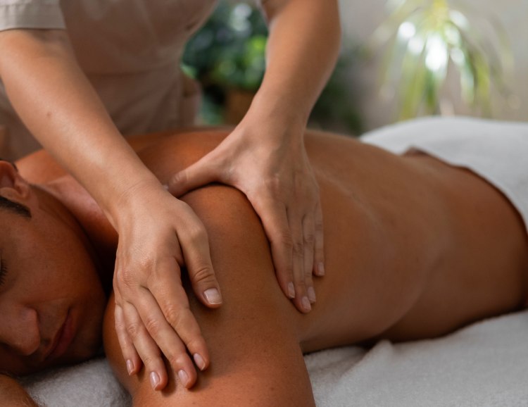 Performing a deep tissue massage on a person's shoulder to relieve pain and muscle tension