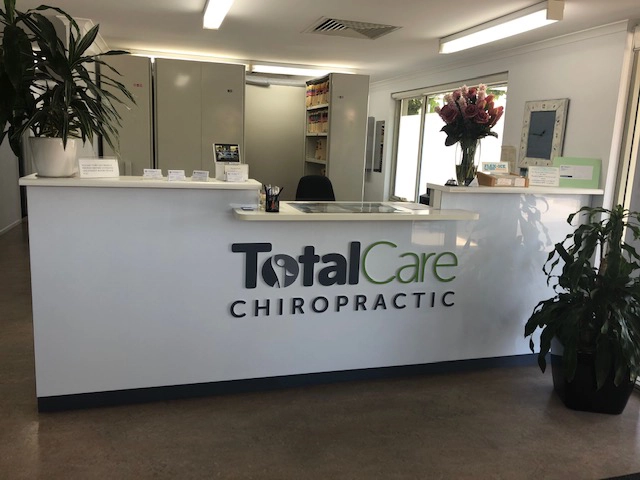 Reception area of our chiropractic clinic with a modern white desk, green plants, and the clinic's logo.